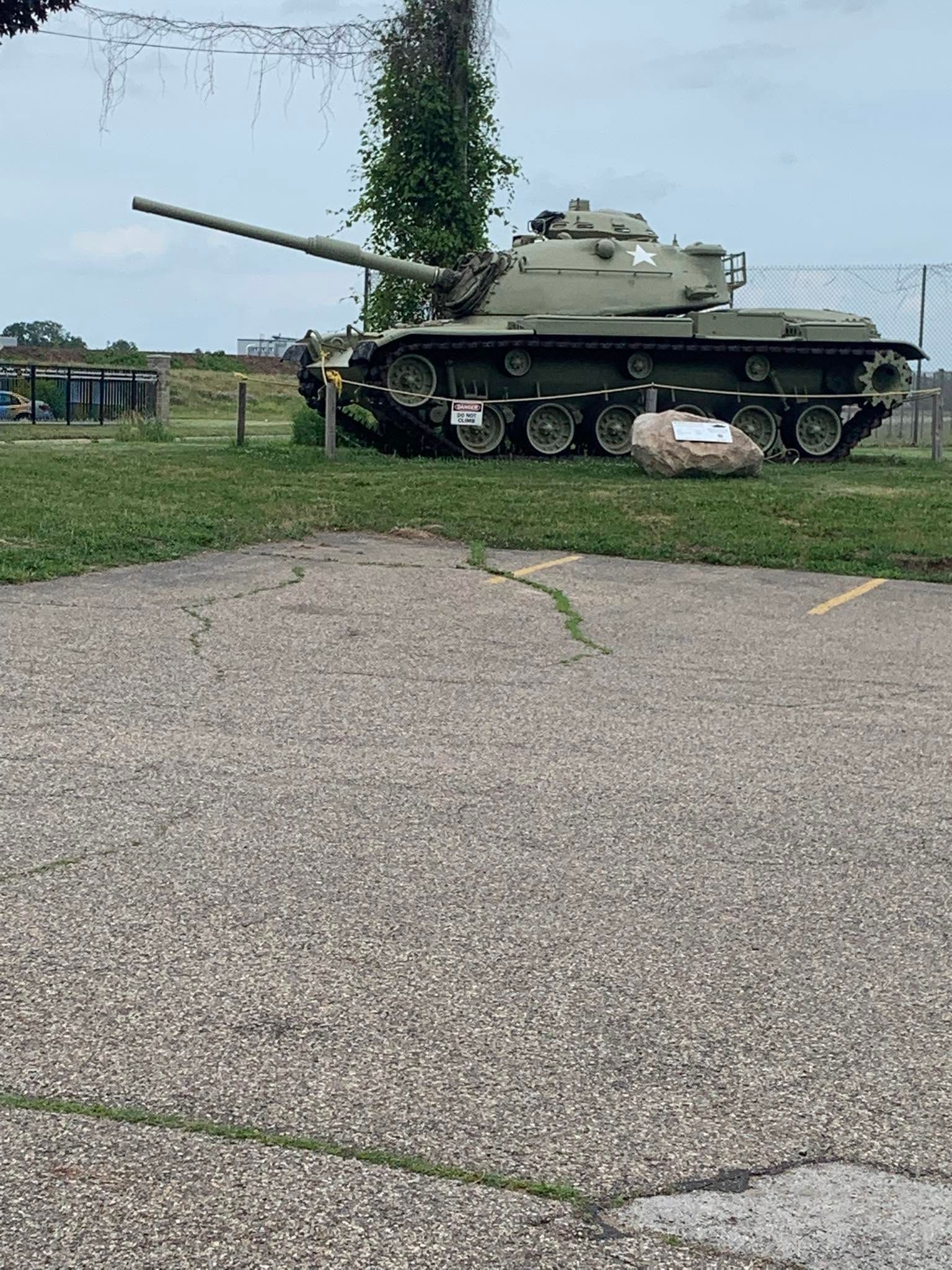 Military tank on display beside a paved path and grass, with a long gun barrel and cloudy sky.