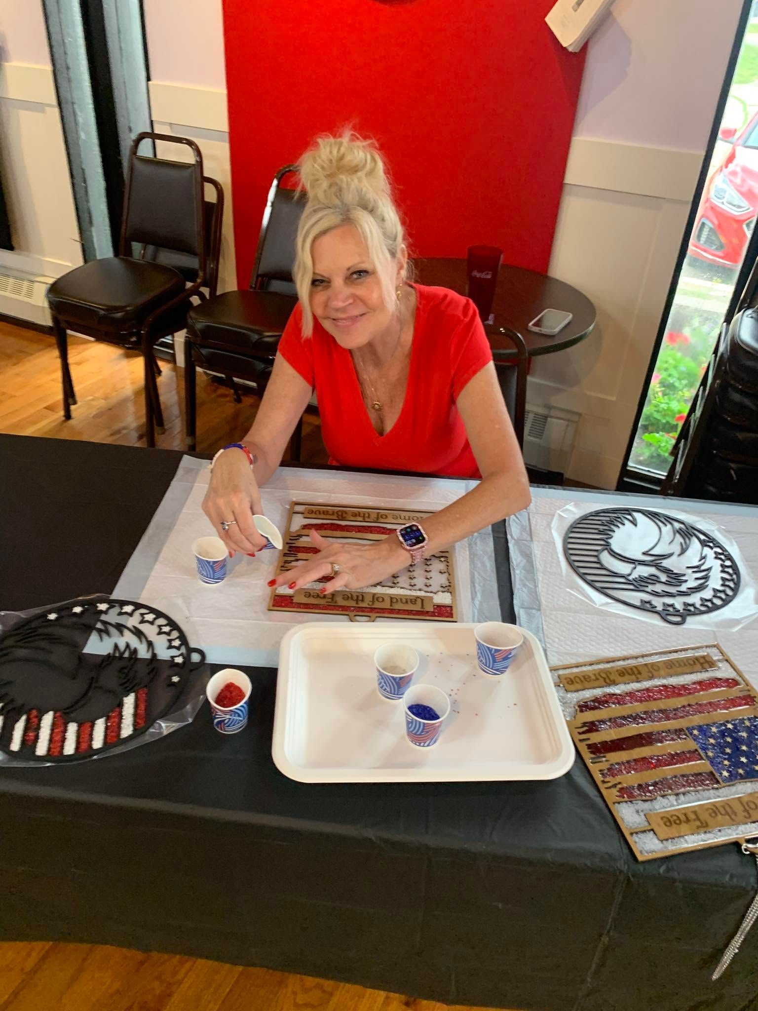 Person at a craft table painting a wooden sign, with supplies spread out on a black-covered table.