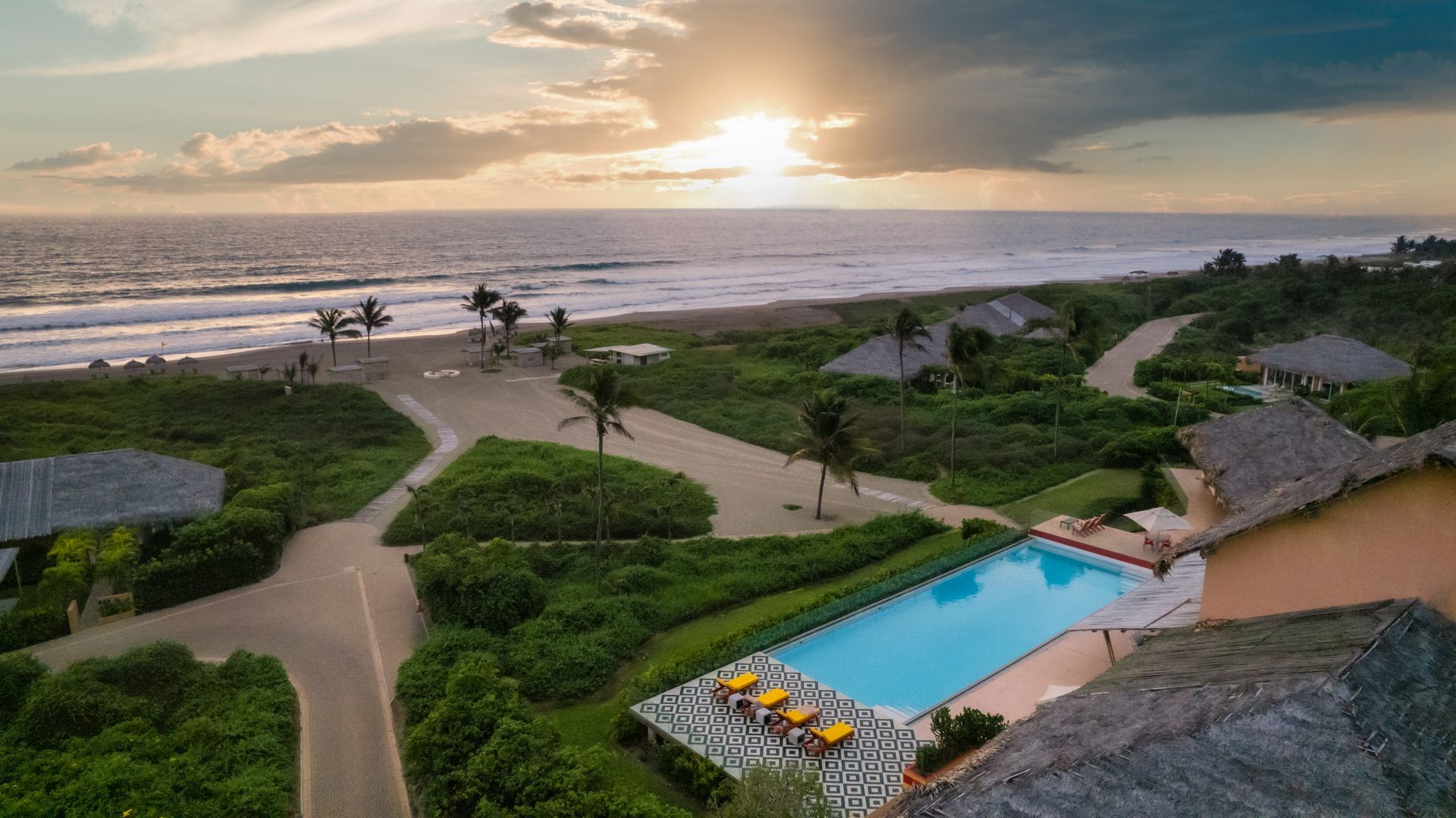 Oceanfront resort with a pool at sunset.