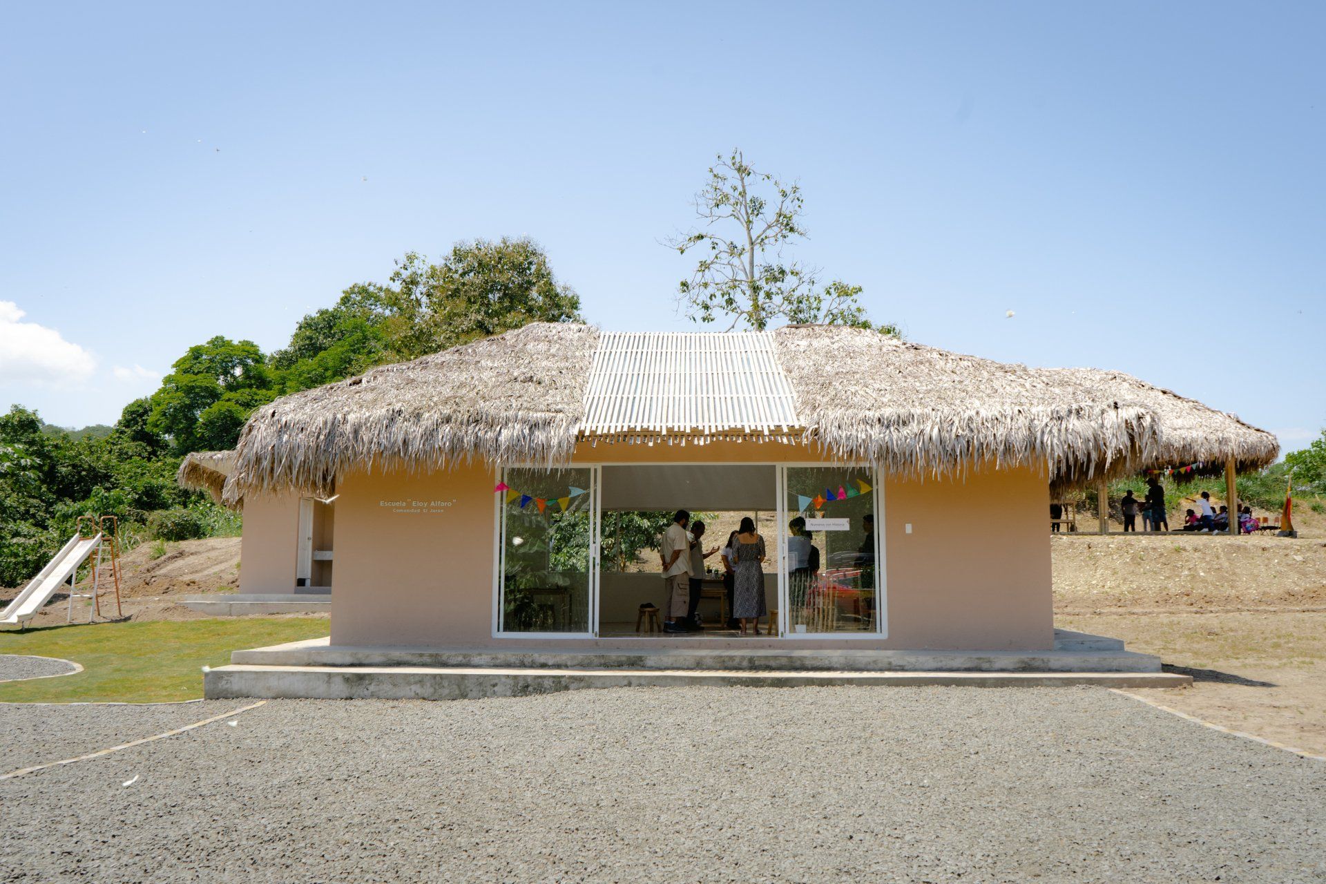 A tan-colored building with a thatched roof and a large window. People are visible inside.