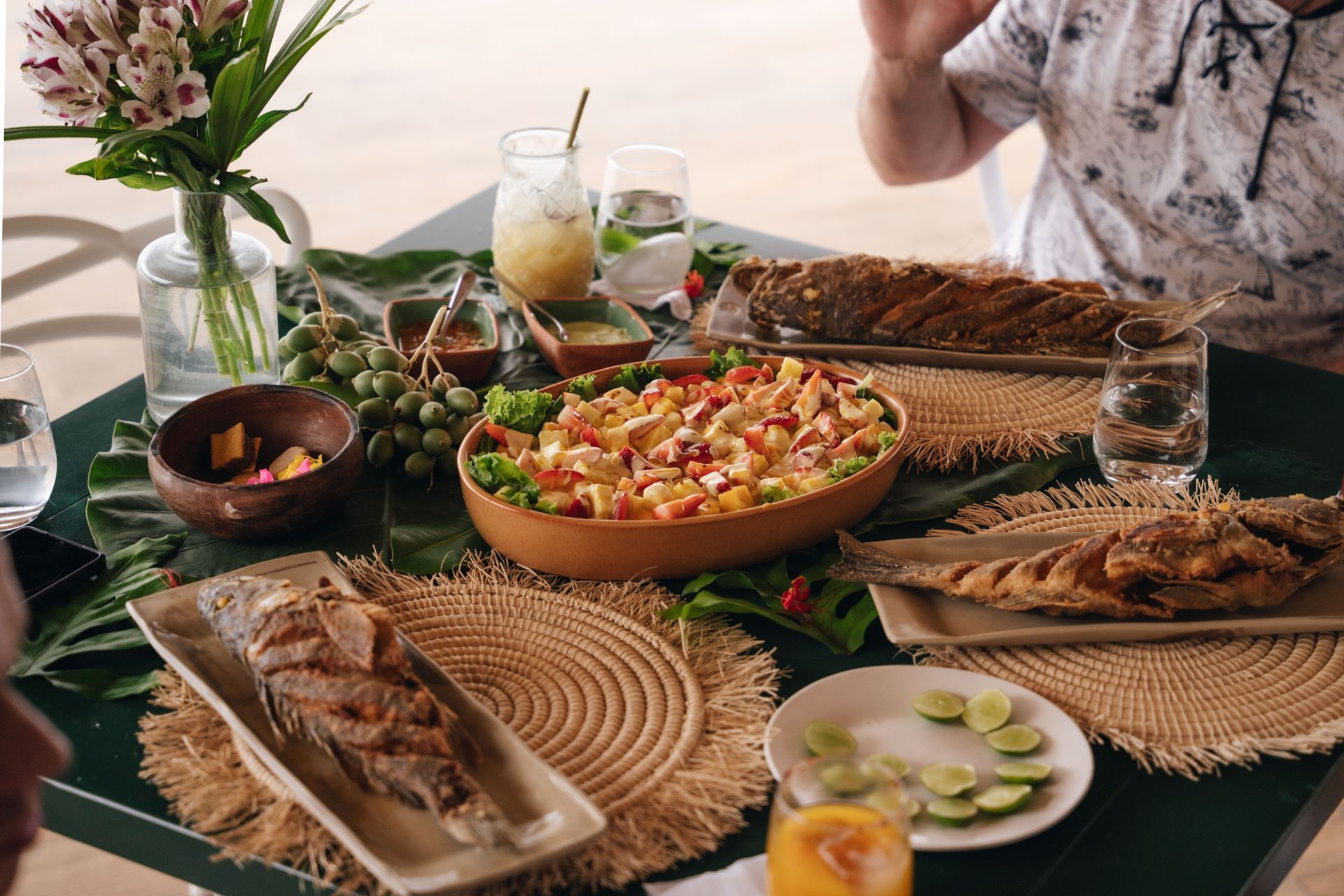 Table set for a meal with fish, salad, fruit, drinks, and two people.