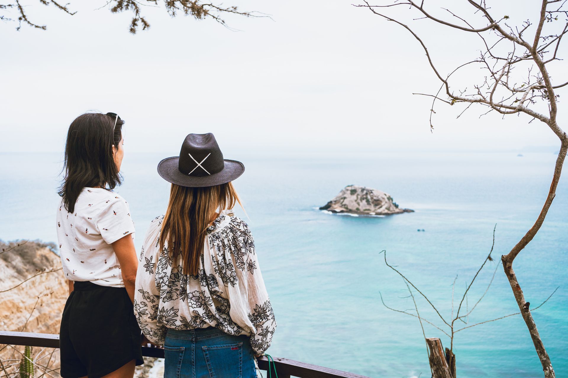 Two women looking at a small island in the ocean from a viewpoint on a cloudy day.