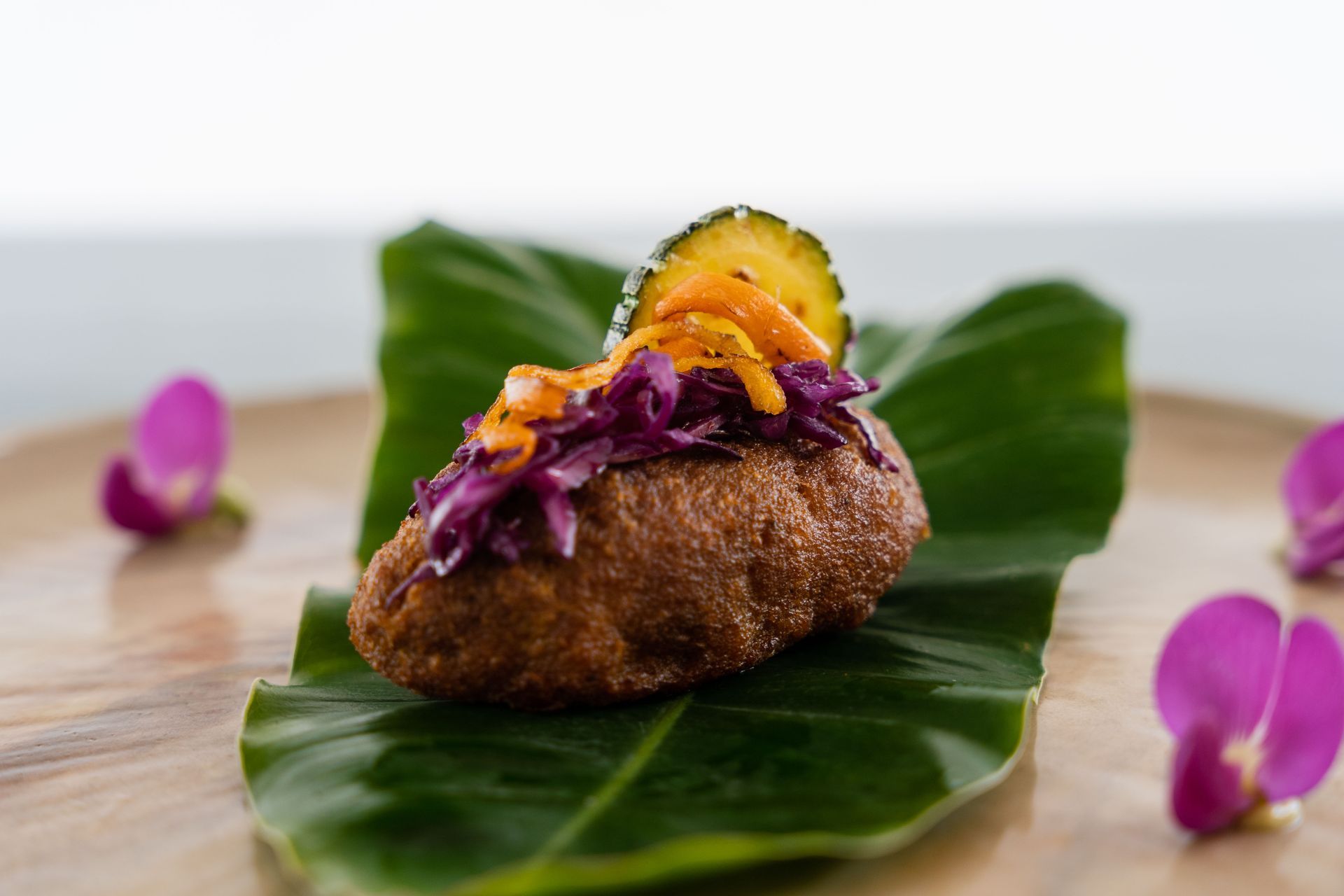Fried dish topped with cabbage, pickle, and sauce, on a leaf-lined plate, with flowers.