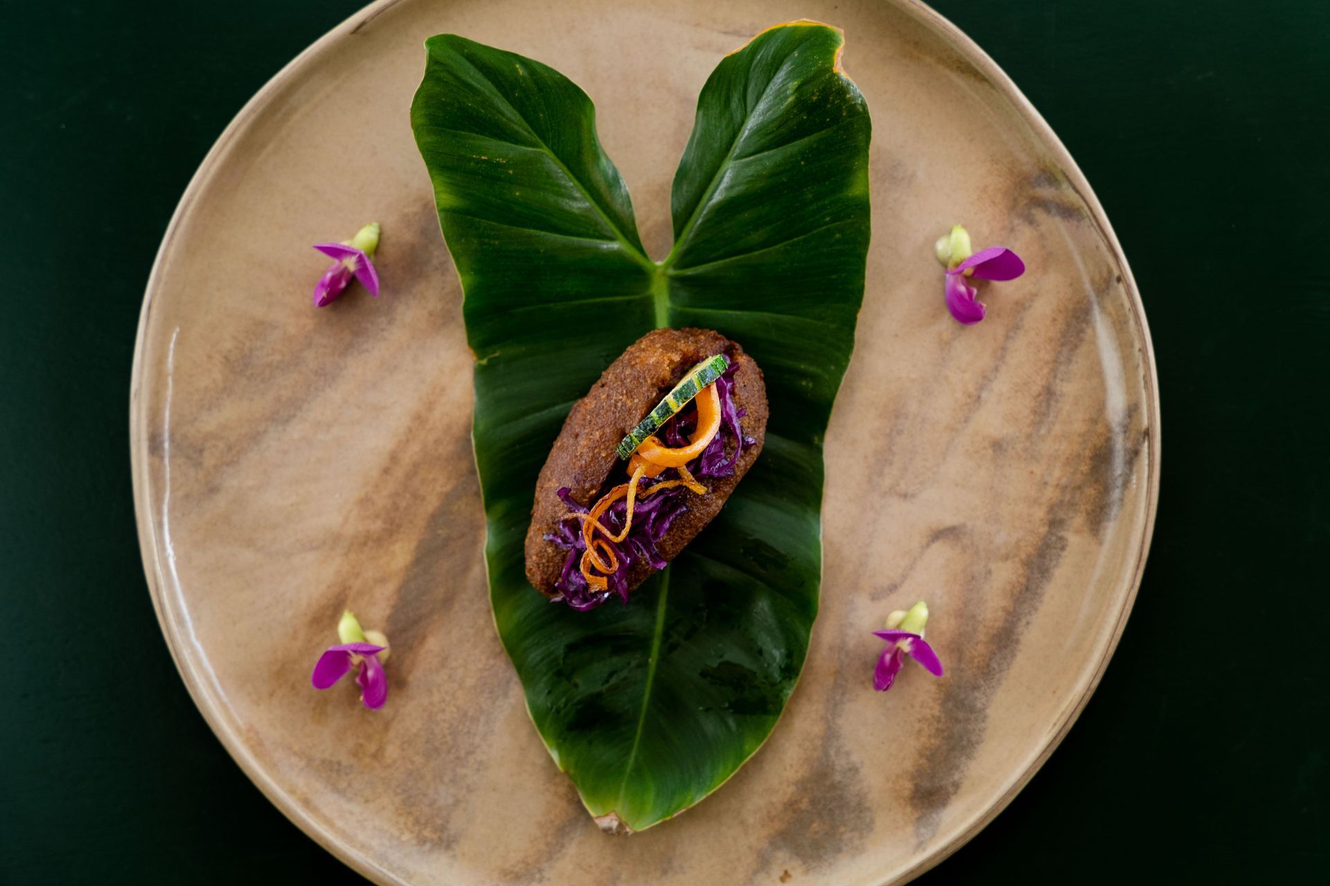 A plate with a dark loaf on a large green leaf, surrounded by small purple flowers.