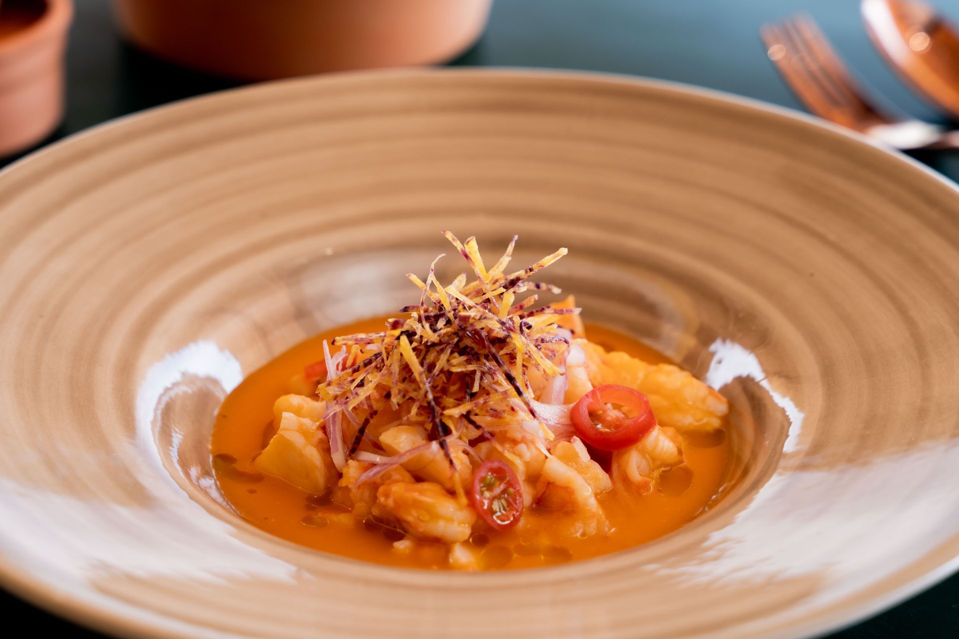 A bowl of ceviche with shrimp, tomatoes, and orange broth.