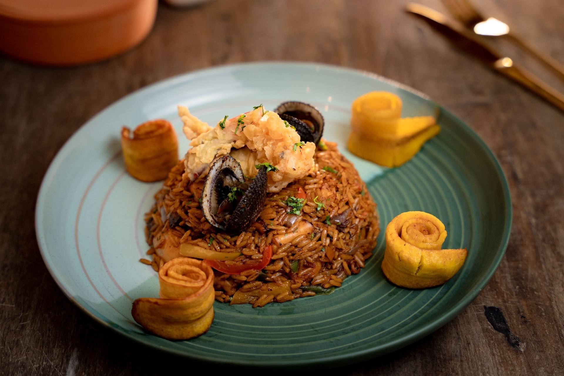 Seafood fried rice on a teal plate, garnished with plantain rolls and seafood.
