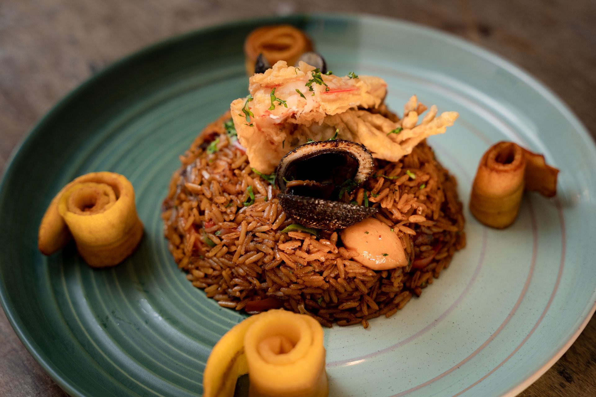 Rice dish, garnished with plantain spirals, served on a teal plate, topped with fried ingredients.