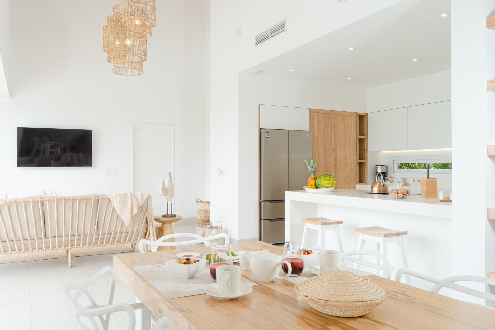 Bright, modern open-plan living space with dining table, white kitchen, and wood accents.