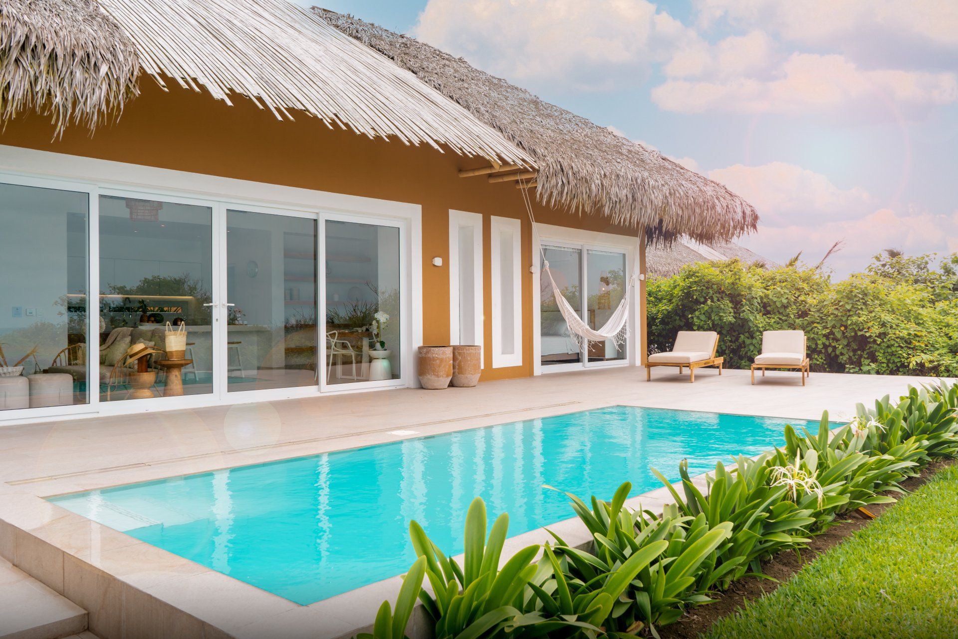 Poolside villa with turquoise pool, thatch roof, and lush greenery.