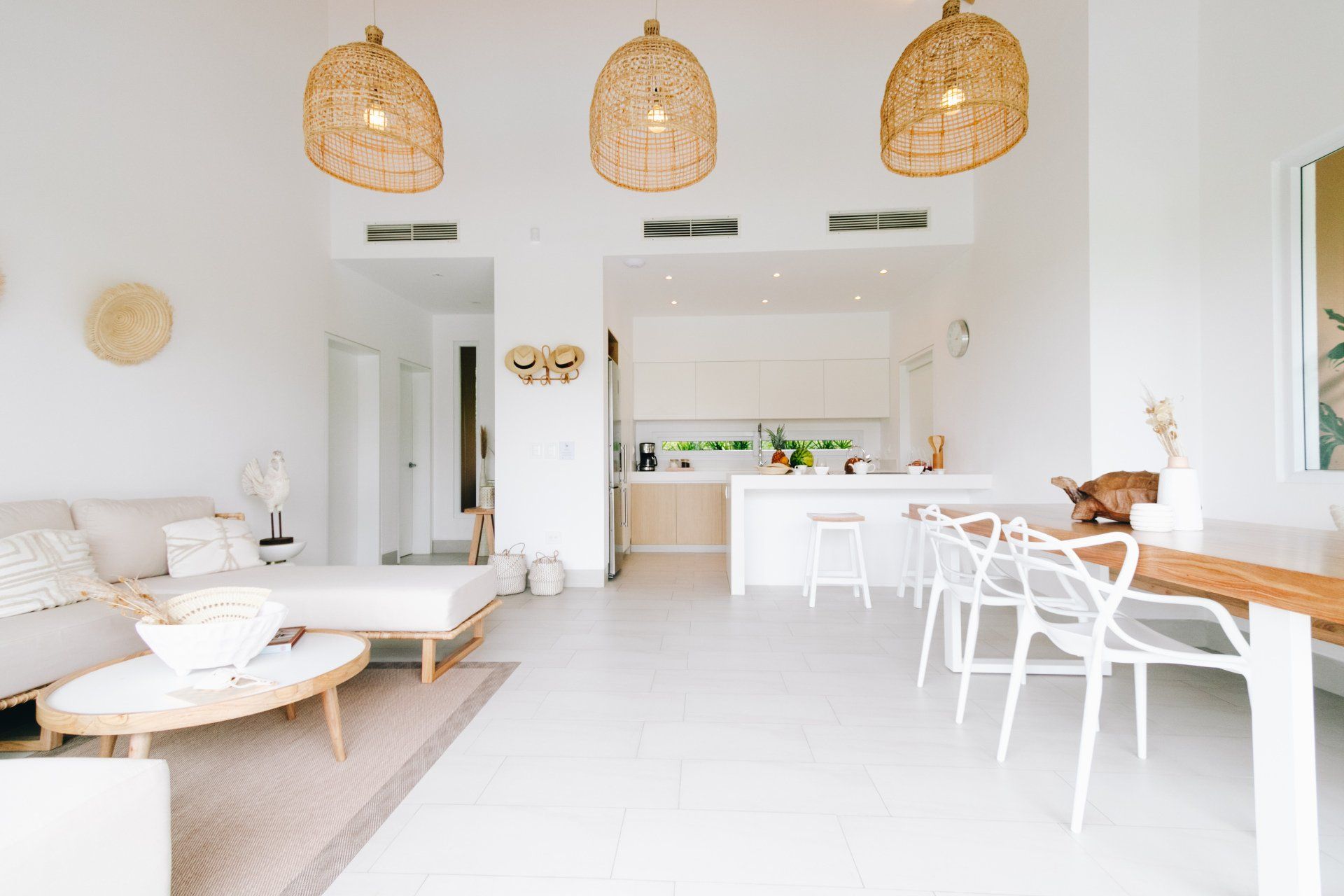 Bright white open-plan living space with kitchen, dining, and seating areas, featuring natural wood and woven accents.