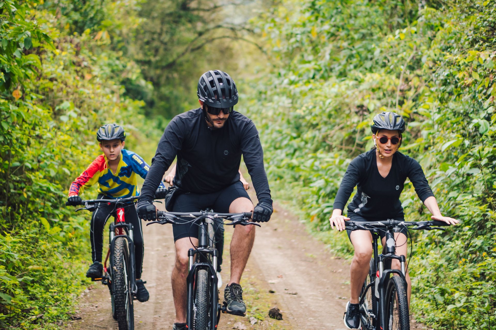 Three cyclists riding bikes on a dirt path through a wooded area.