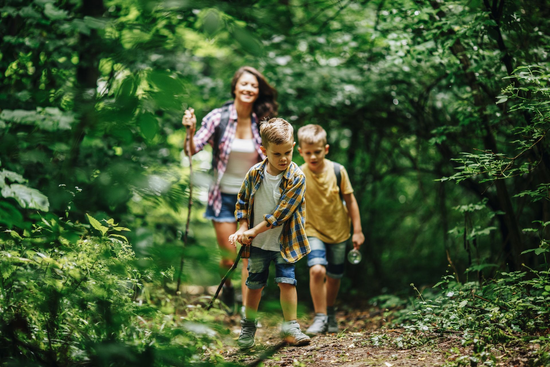 Woman and two children hiking through a green forest, smiling.