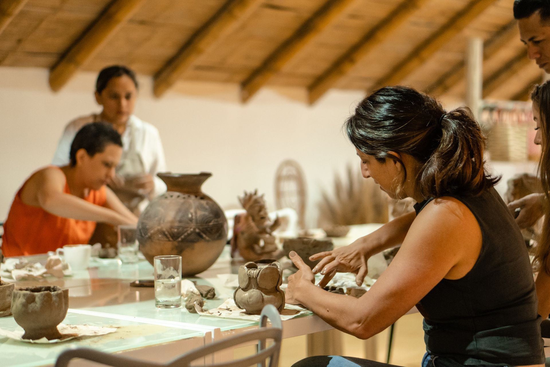 People crafting pottery at a table; interior setting with natural light.