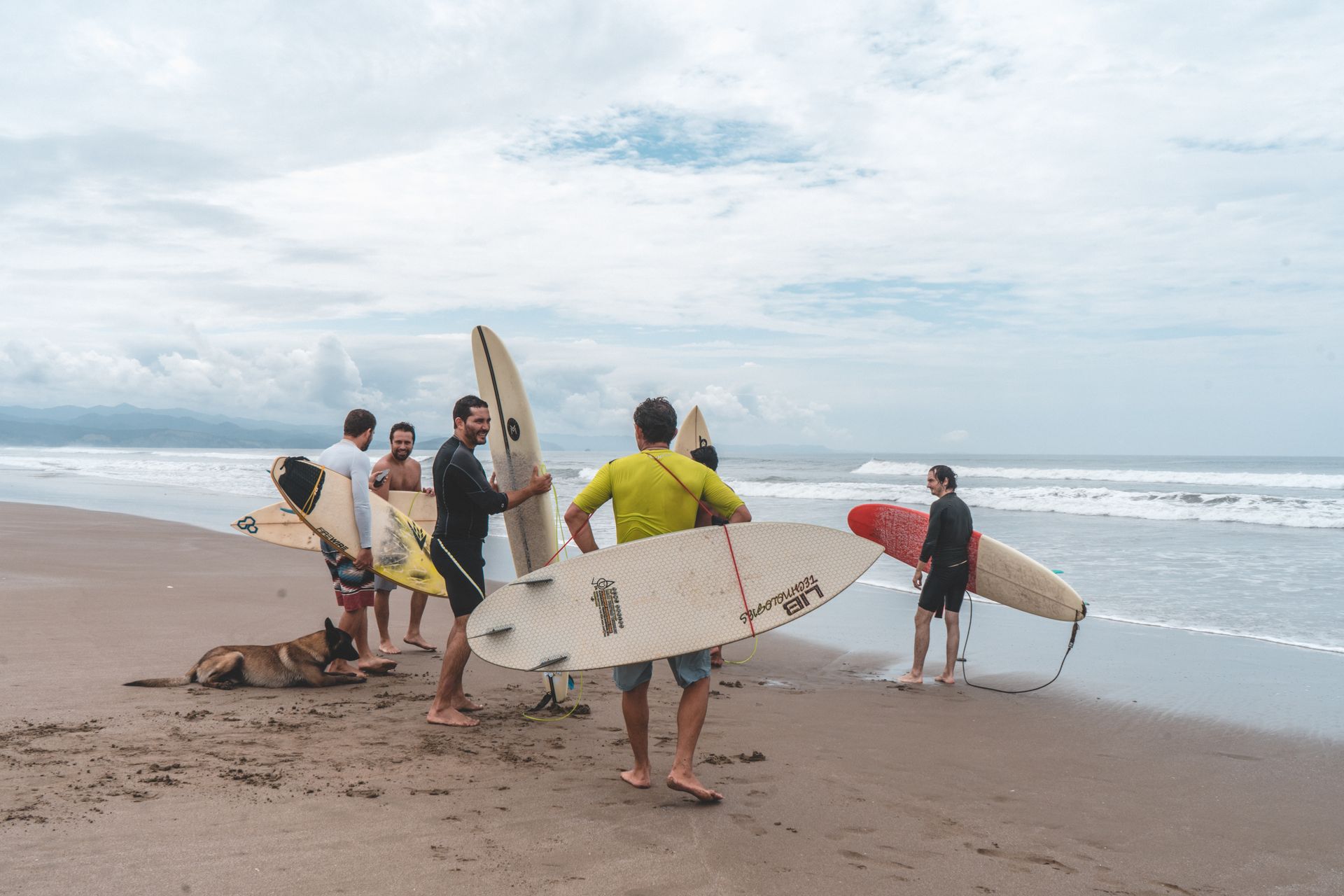 A group of surfers with boards on a beach, preparing to enter the ocean under a cloudy sky.