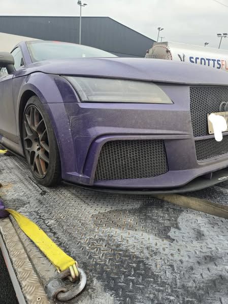 Purple Audi TT sportscar on a tow truck, overcast day.