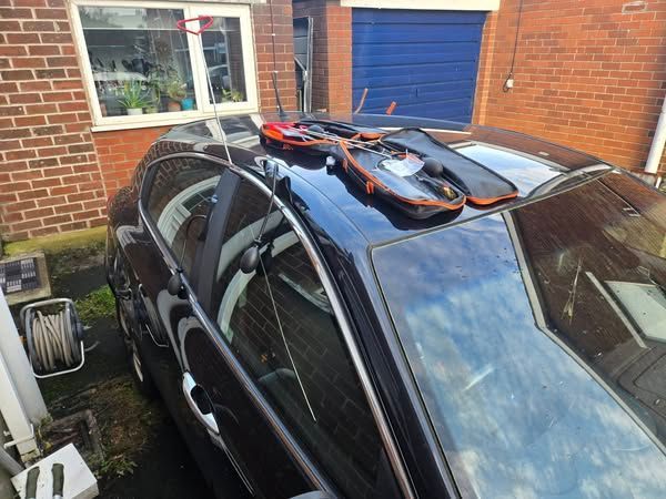 Black car with orange and black object on the roof, near a brick building.