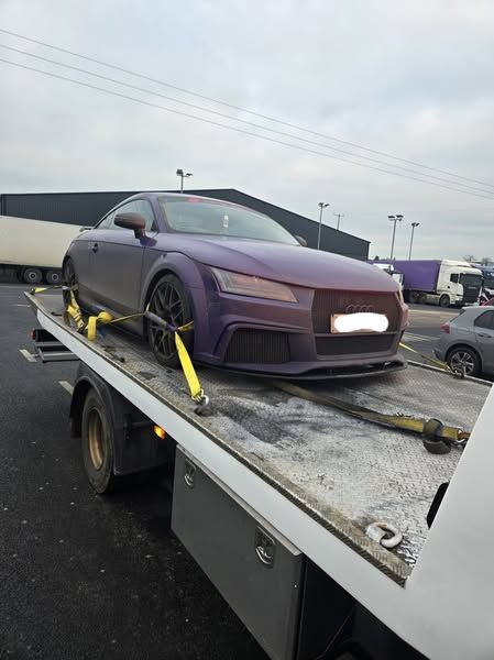 Purple Audi TT sportscar on a tow truck, overcast day.