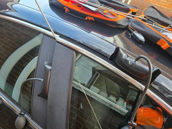 Black car with orange and black object on the roof, near a brick building.