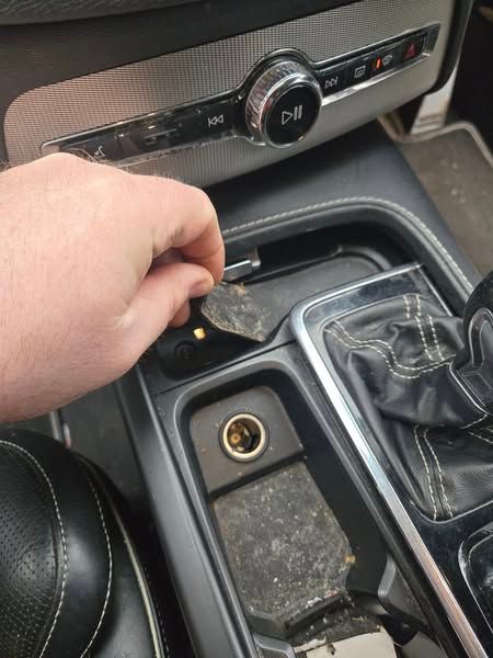 Car interior: center console with gear shift, power outlet, and control panel. Black and silver.
