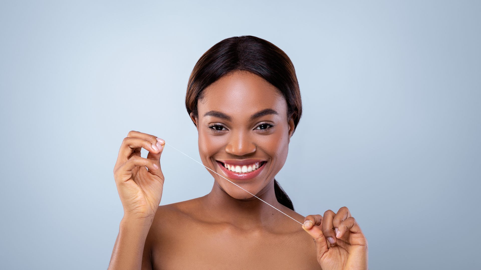 A woman with a bright smile using dental floss to maintain good oral health. A woman with a bright smile using dental floss to maintain good oral health.