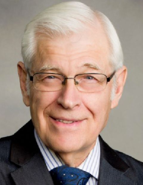 Headshot of an older person with white hair and glasses, wearing a pinstriped shirt and tie against a gray background.