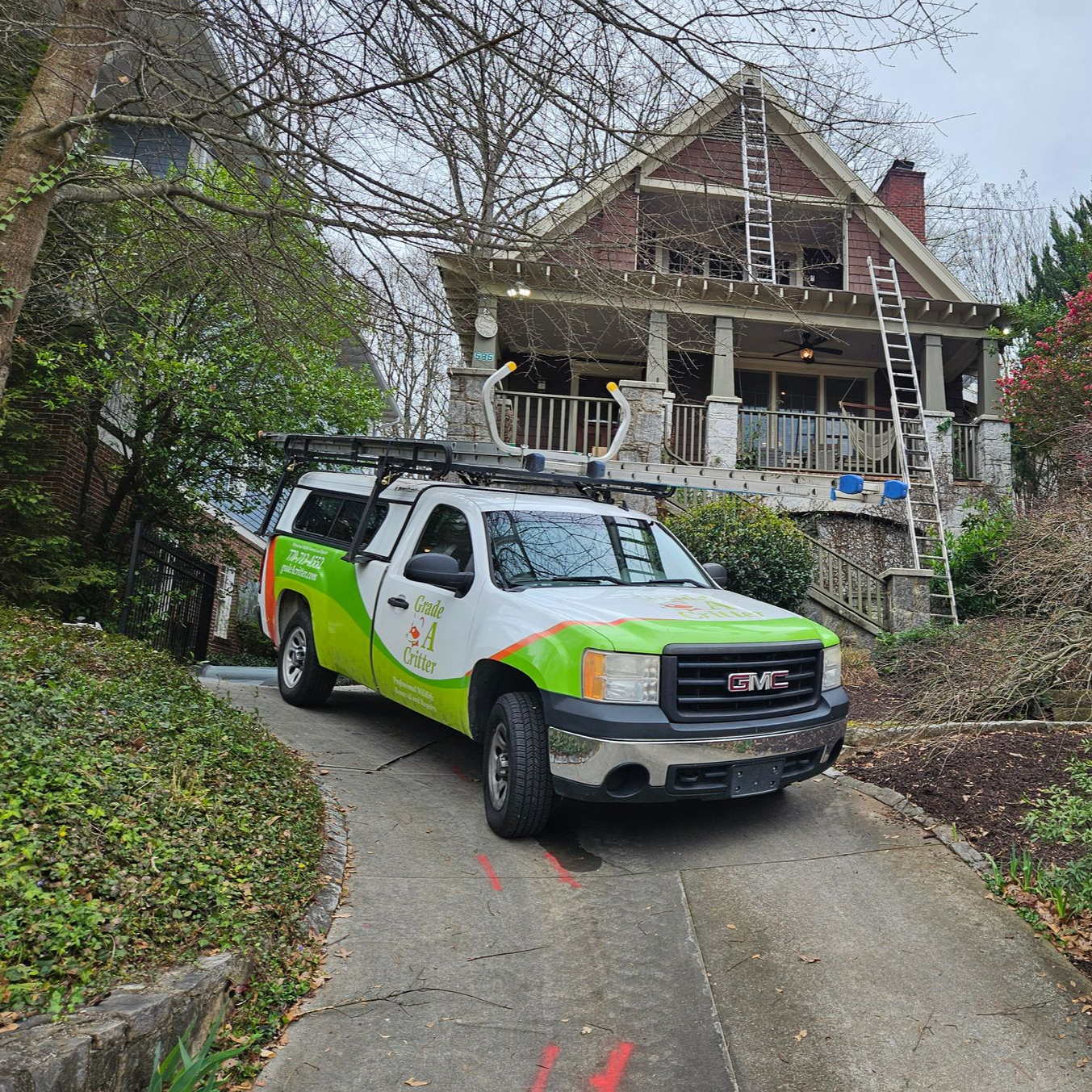 A white and green work truck parked in the driveway of a house undergoing exterior renovation.