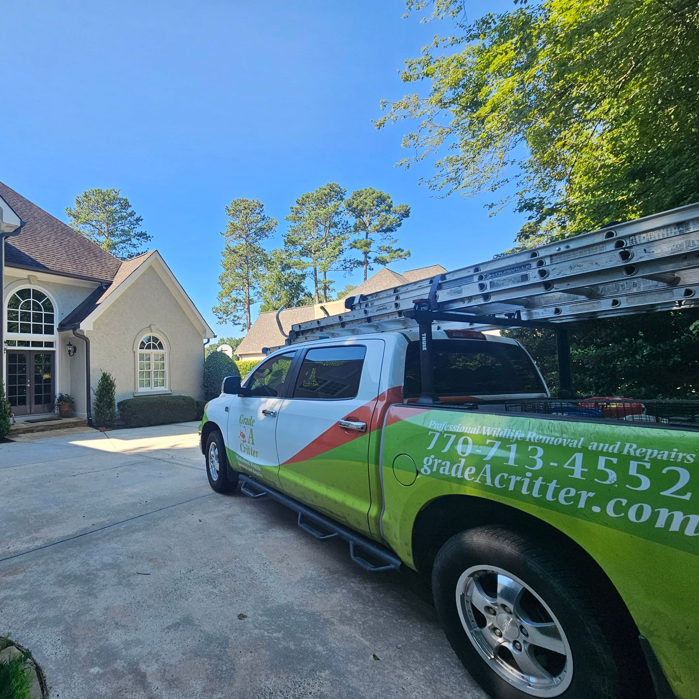 A white and lime green pickup truck parked in a driveway in front of a house, featuring text for wildlife removal services.