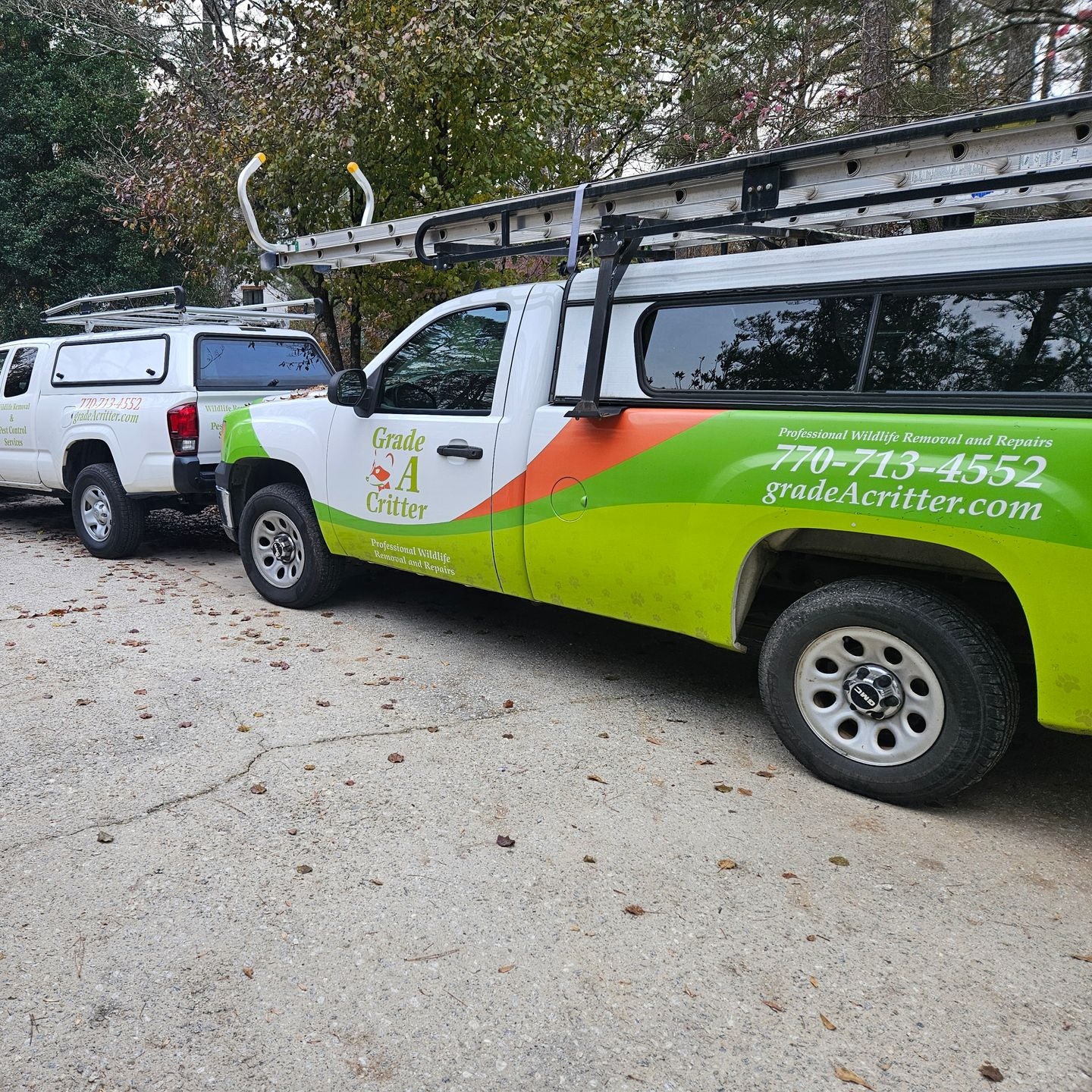 Two white pickup trucks with ladders and green and orange branding for