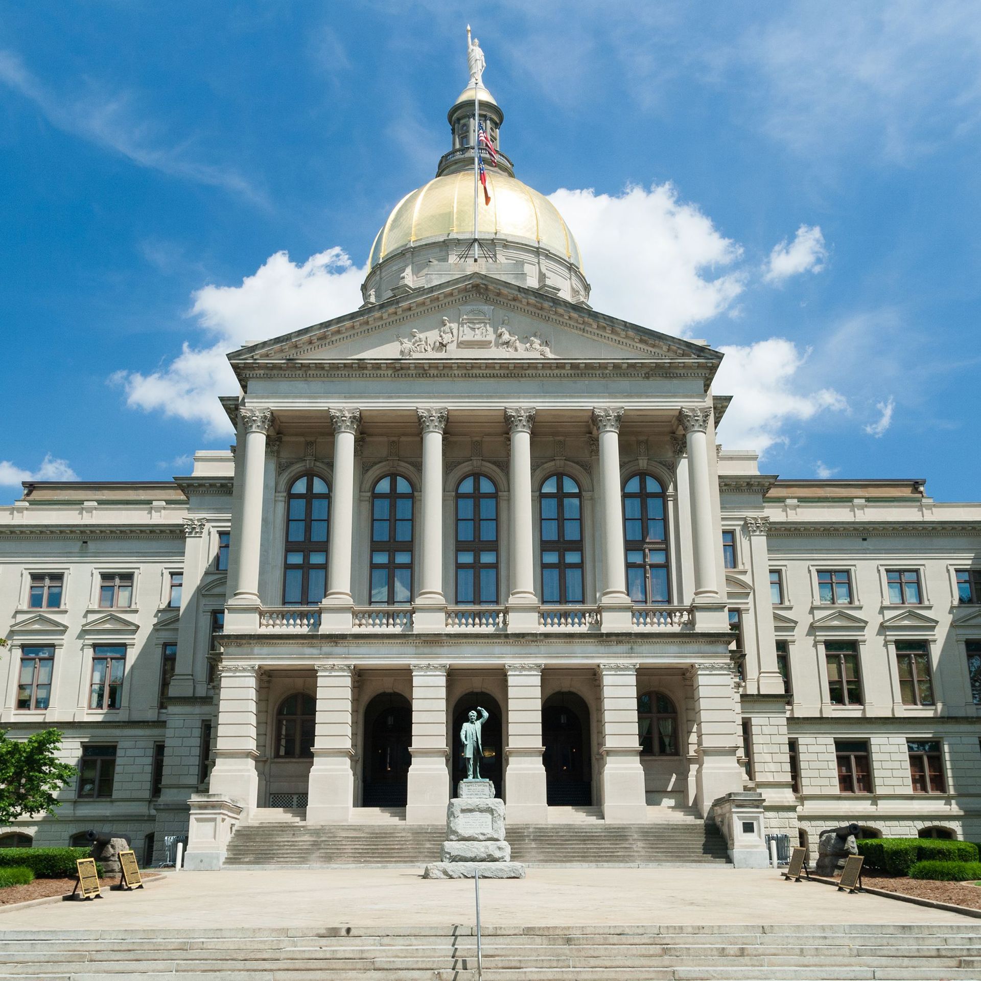 State capitol building with a gold dome, grand columns, and a central statue under a blue sky.