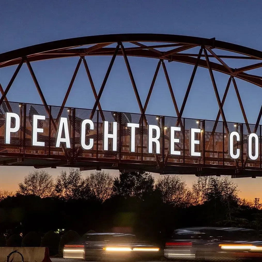 Lit Peachtree Co sign on a metal bridge at dusk with car light streaks below