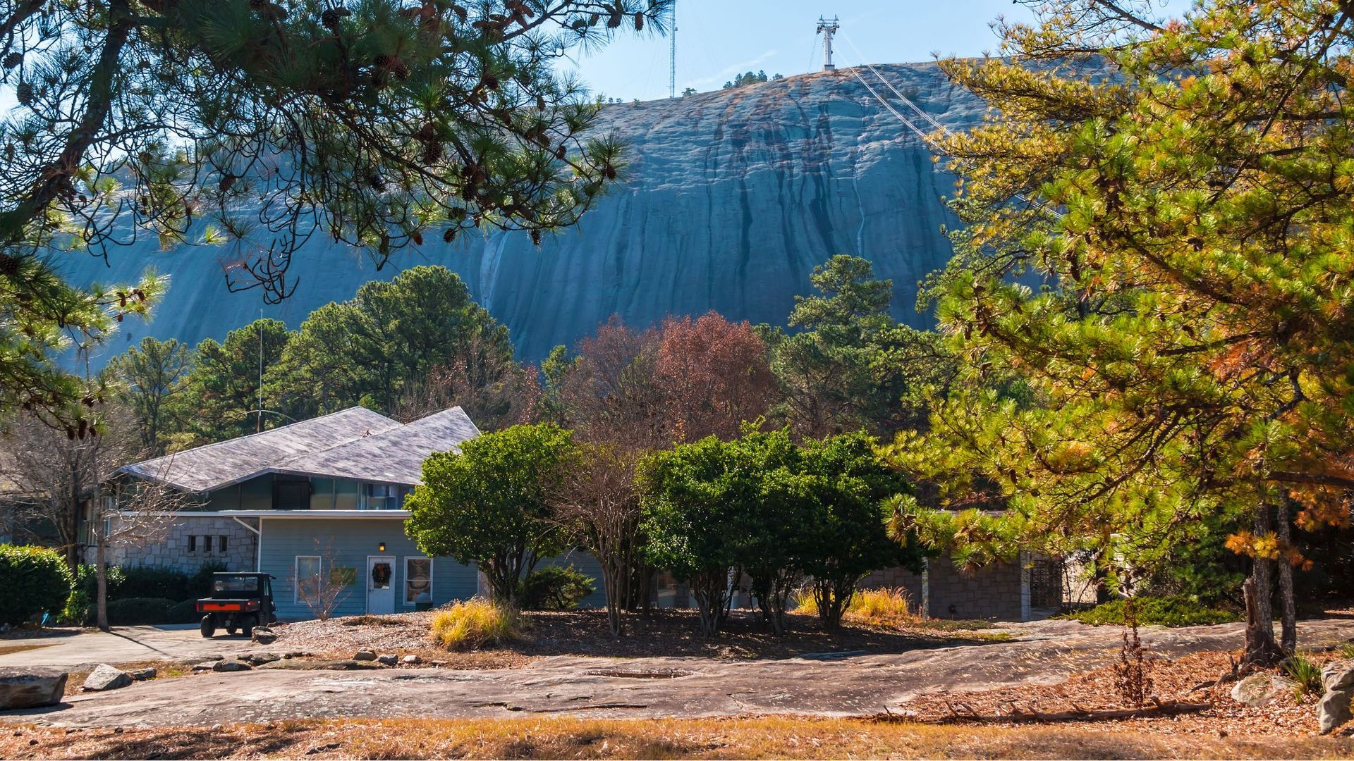 Wide green lawn in front of a massive gray rock cliff with trees and a small waterfall basin.