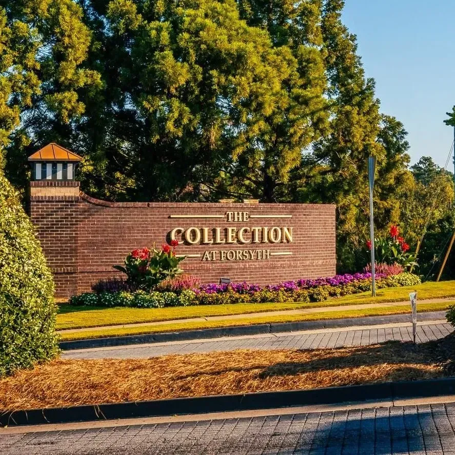 Stone entrance sign for “The Collection at Forsyth” surrounded by flowers and trees on a sunny day