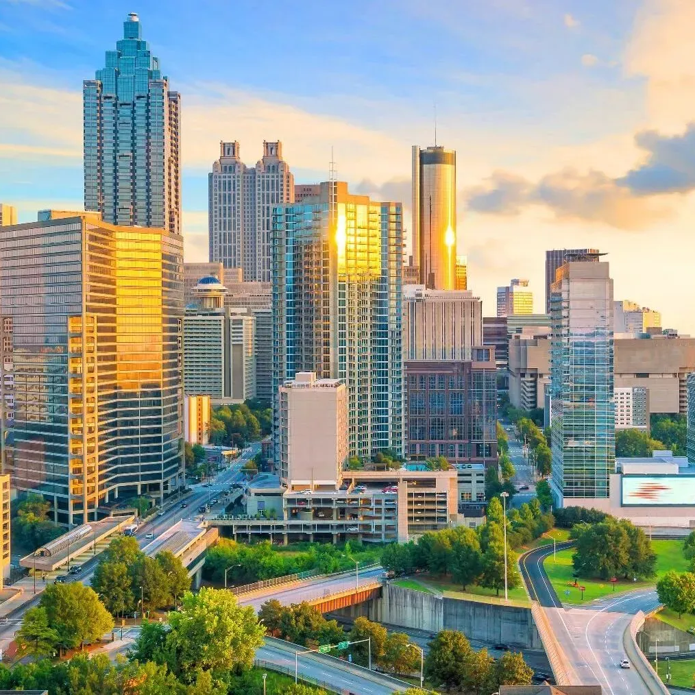 Modern city skyline at sunset with tall glass skyscrapers, blue sky, and a green park in the foreground