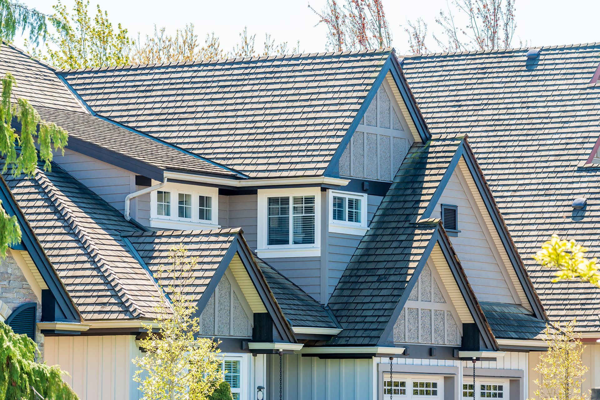 Close-up of a gray-shingled house roof with dormer windows and gables in bright daylight