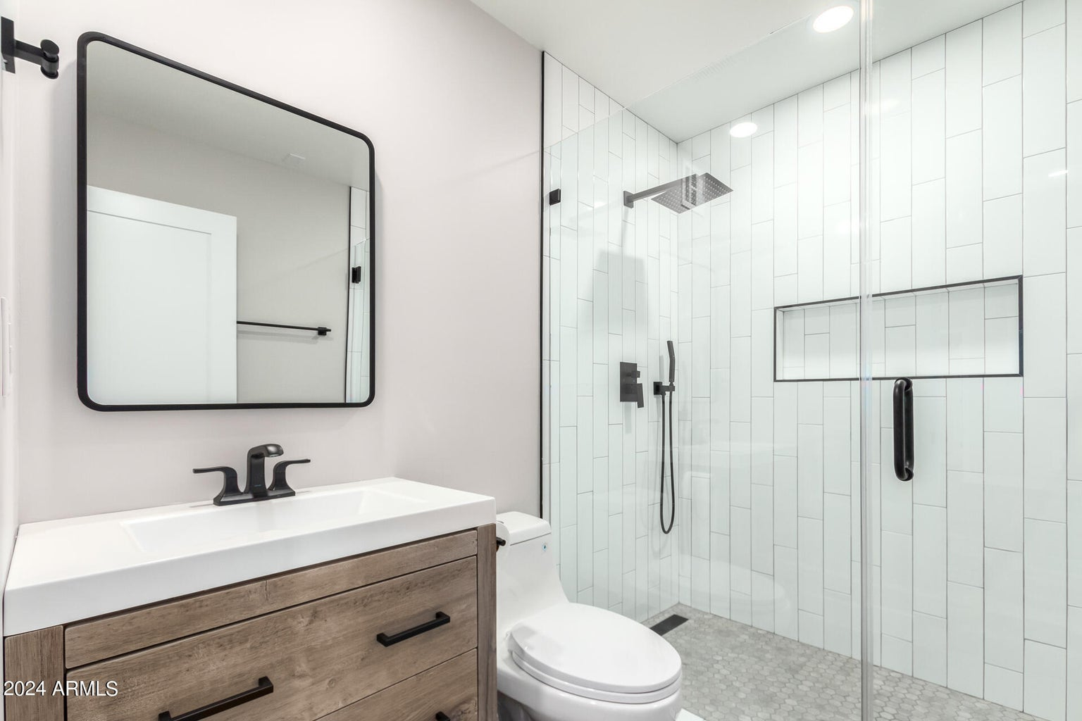 Modern bathroom with white, tiled shower, wood vanity, and black fixtures.