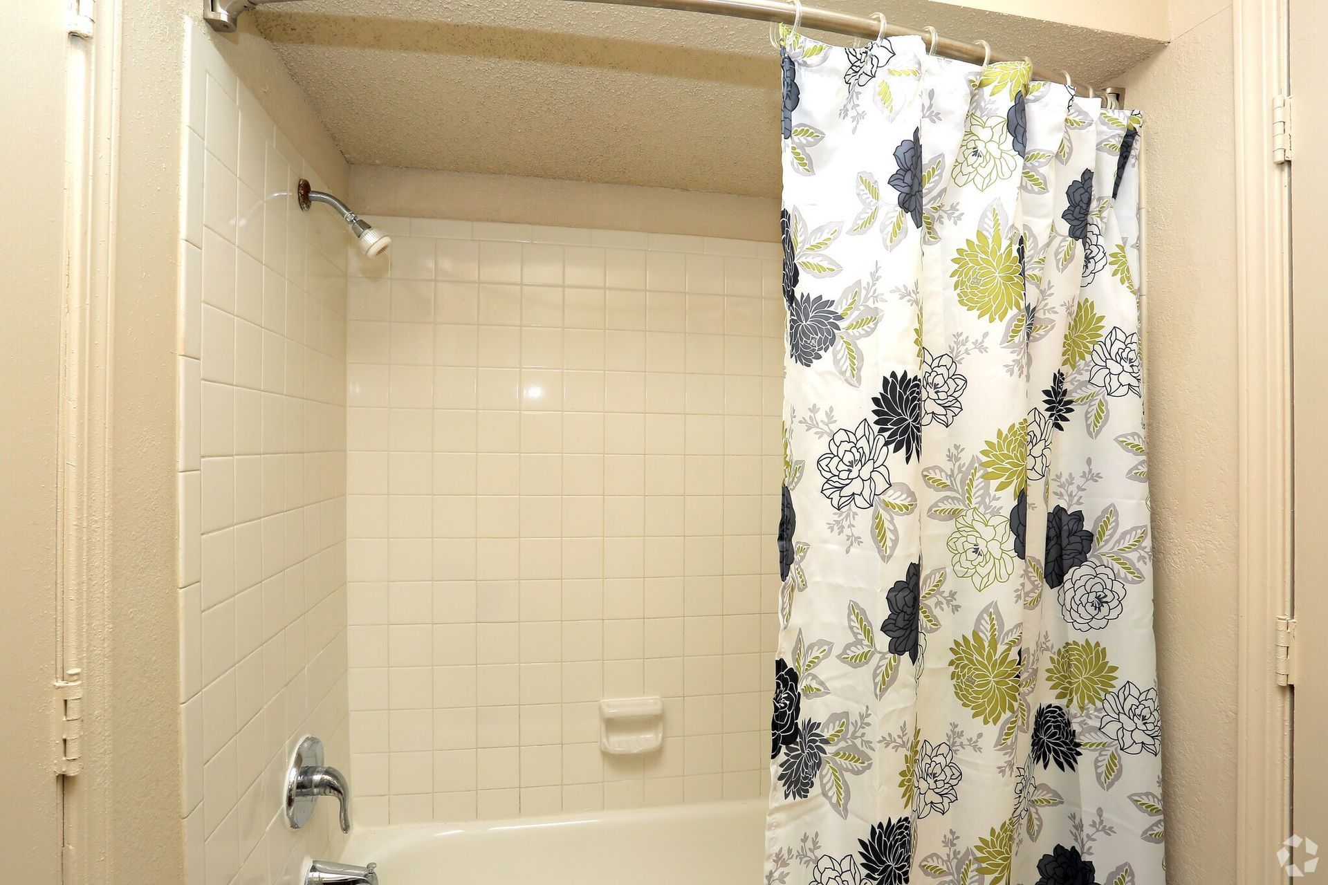 A white tiled bathtub and shower with a curtain featuring a floral pattern in shades of green, black, and white.
