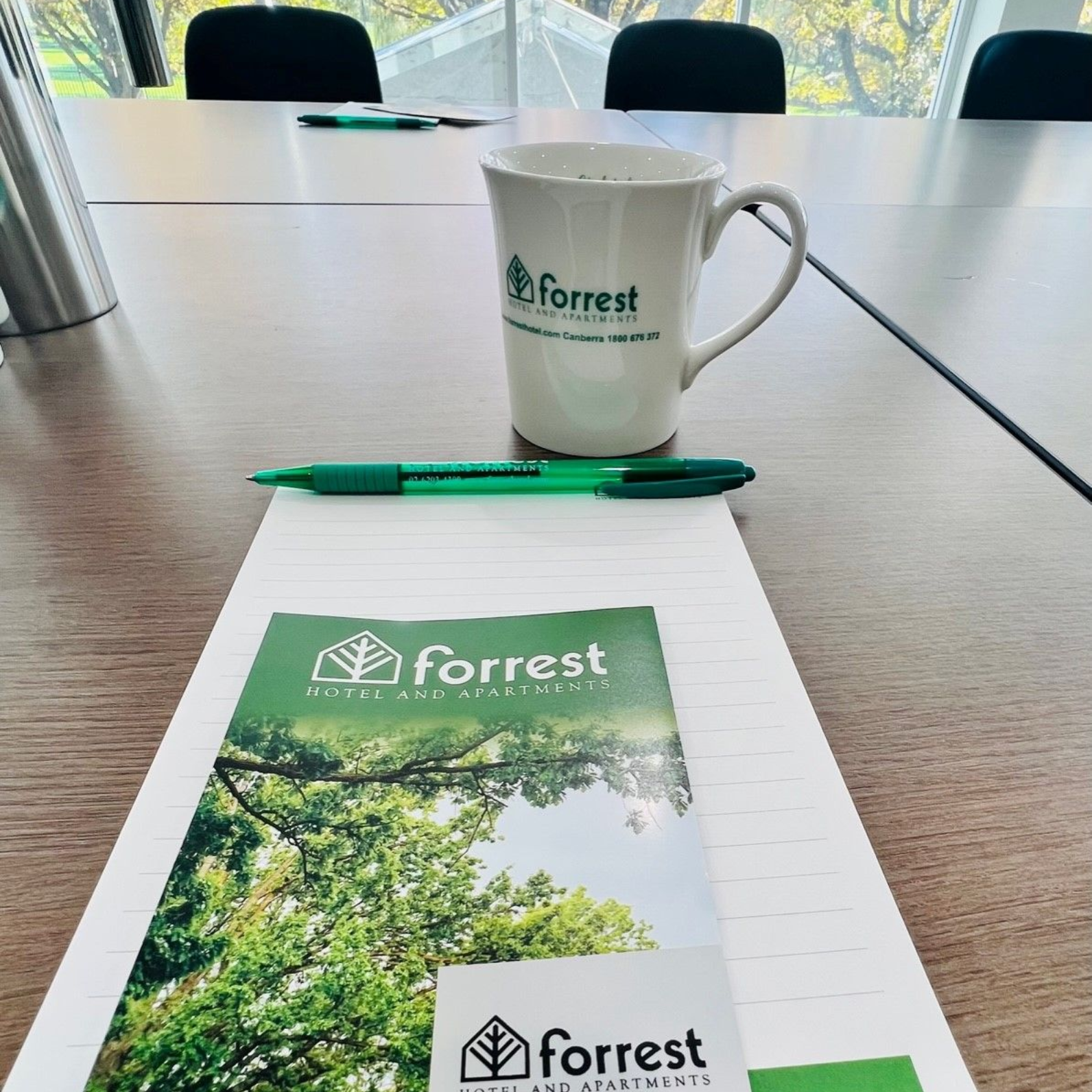 Forrest-branded mug, pen, and brochure on a table in a bright conference room.