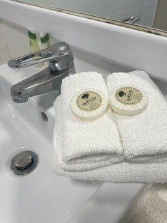 White towels with two small round toiletries on a bathroom sink beside a chrome faucet.
