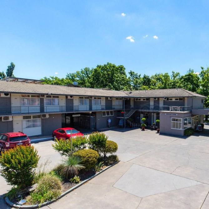 Motel-style two-story building with red cars parked in front on a sunny day
