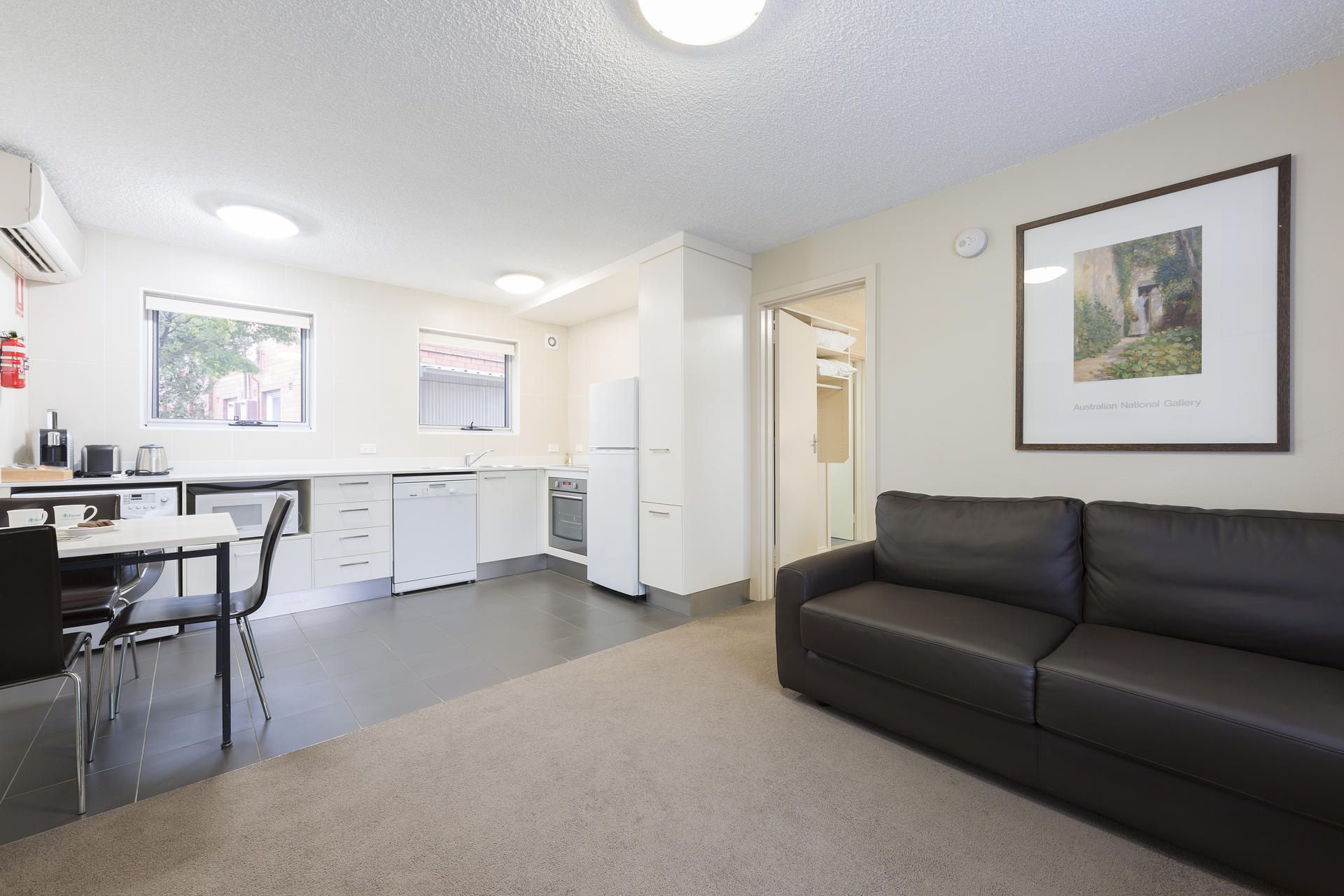 Bright apartment living room with black sofa, small dining table, and kitchenette by large windows