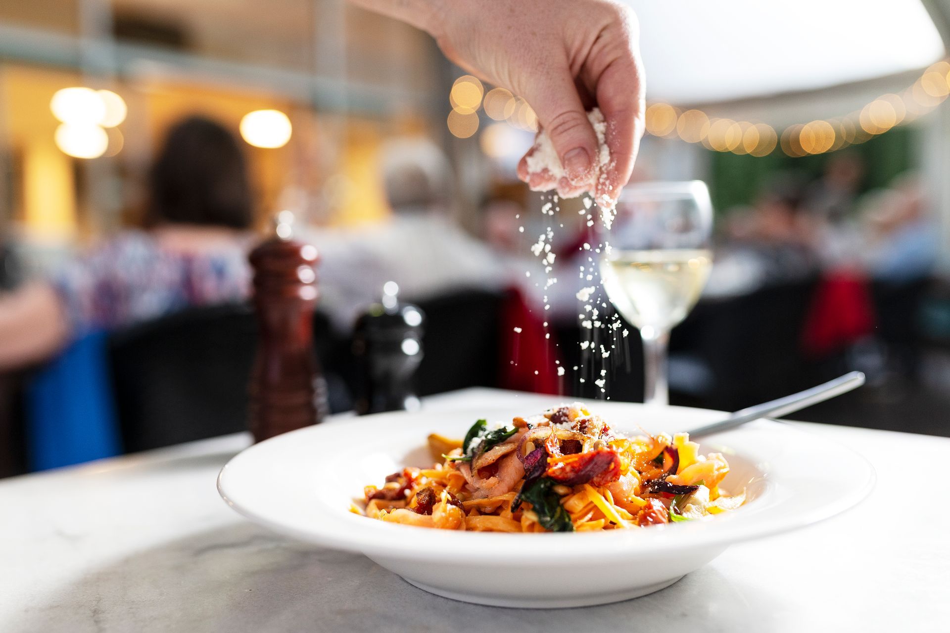 Hand sprinkling seasoning over a plated pasta dish in a restaurant