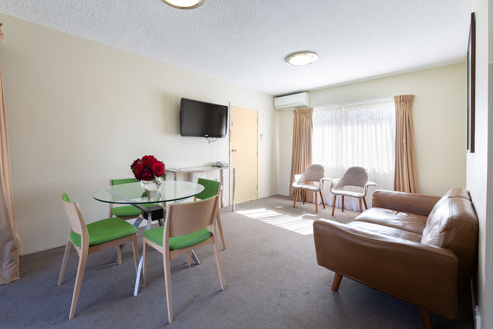 Bright apartment living room with sofa, dining table, chairs, TV, and sunlit window curtains