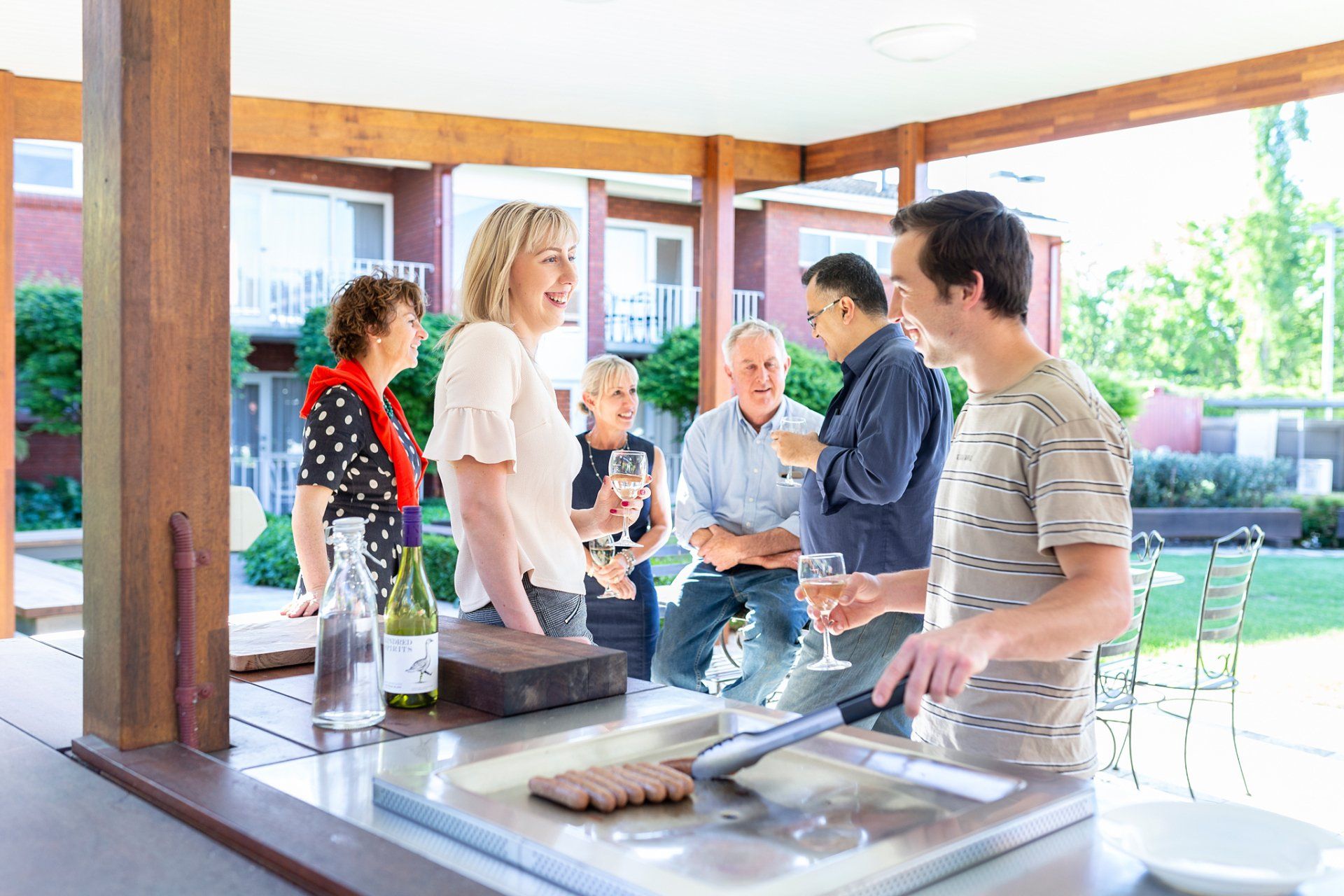 People gathered around a buffet table in a bright outdoor pavilion, serving food and chatting.