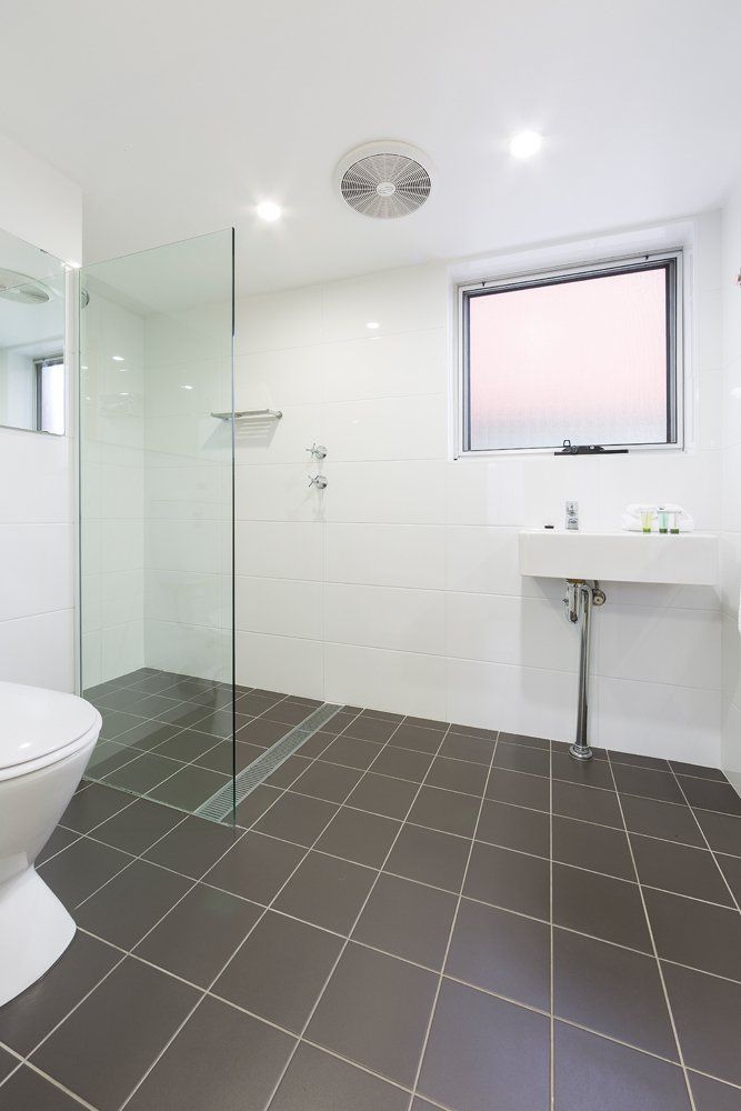 Modern white bathroom with glass shower, gray tiled floor, and sink under a pink-tinted window