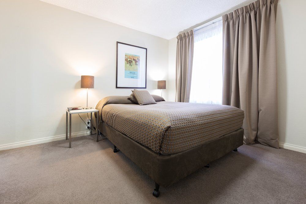 Minimal bedroom with neatly made bed, bedside lamp, framed wall art, and closed curtains