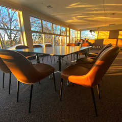 Modern conference room with a long table, black and orange chairs, and warm sunlight through large windows