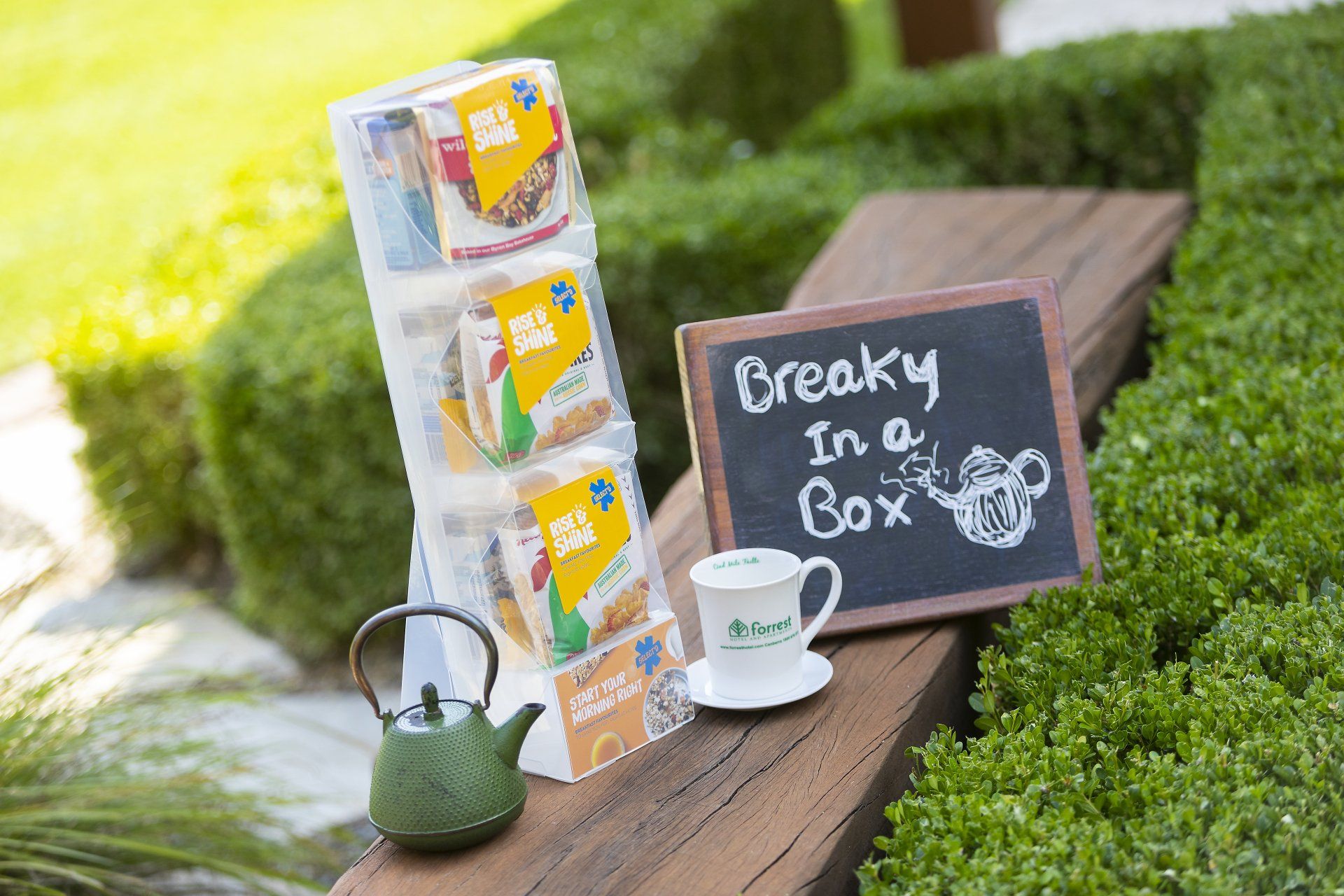Tea display with stacked boxes, a chalkboard reading “Break in a Box,” teapot, and cup on a wooden bench