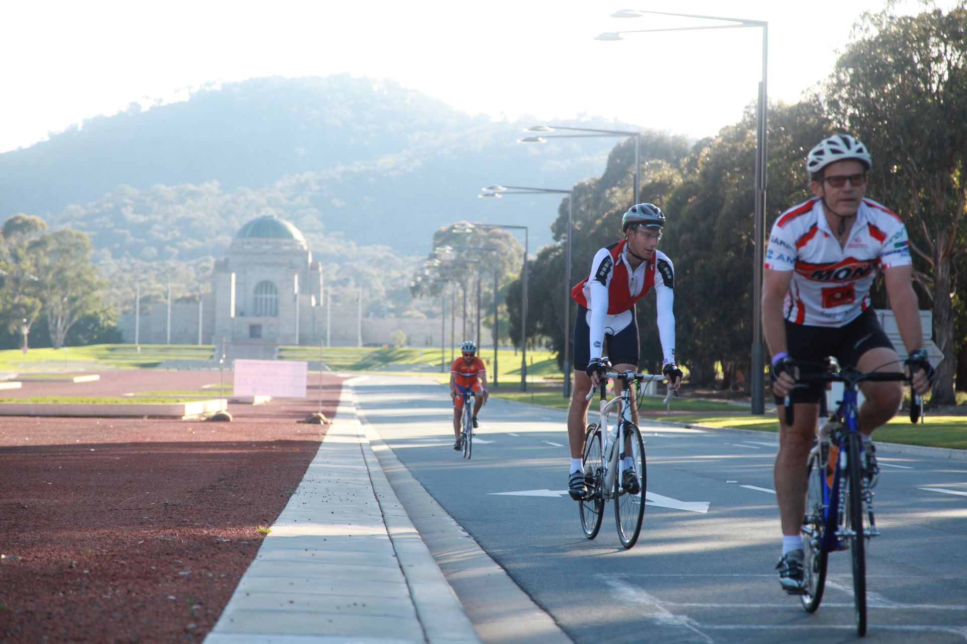 Cyclists riding on a sunlit road near a monument and hills in the background