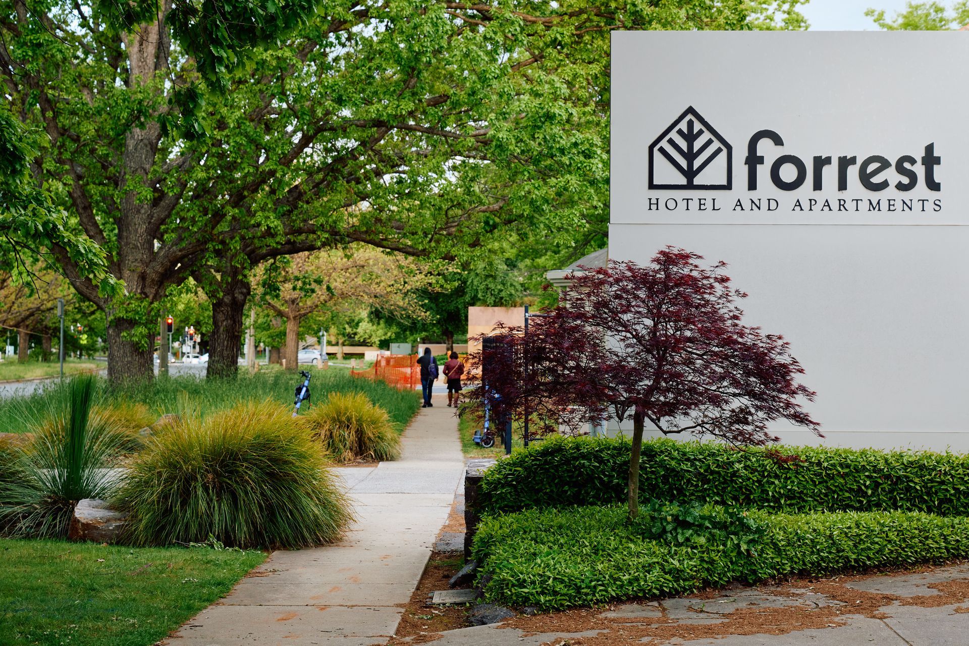 Forest Hotels and Apartments sign beside a landscaped sidewalk with trees and shrubs