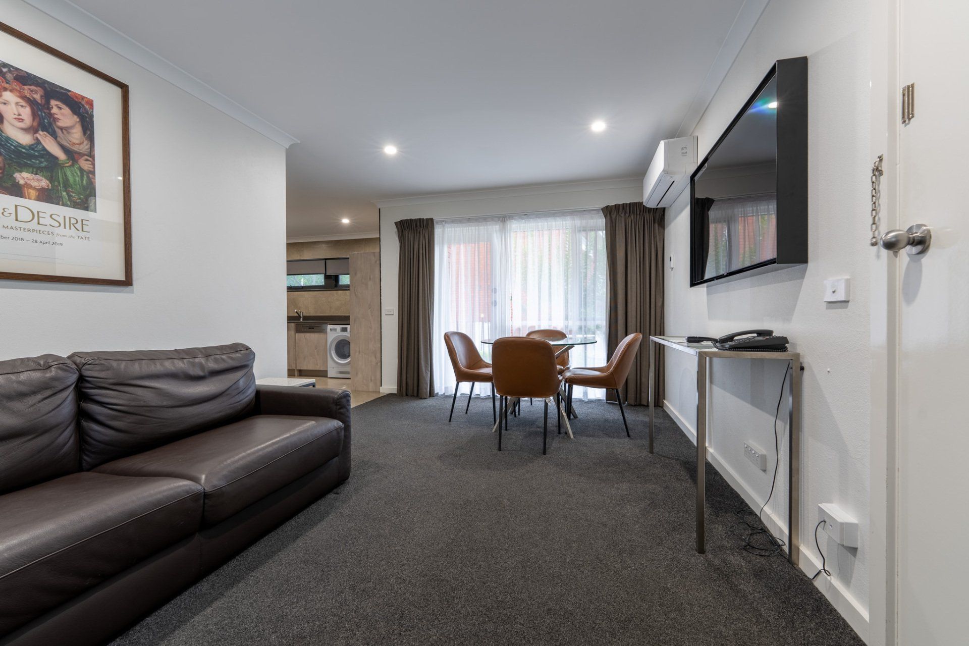 Modern living-dining room with dark sofa, round table, wall-mounted TV, and large window curtains